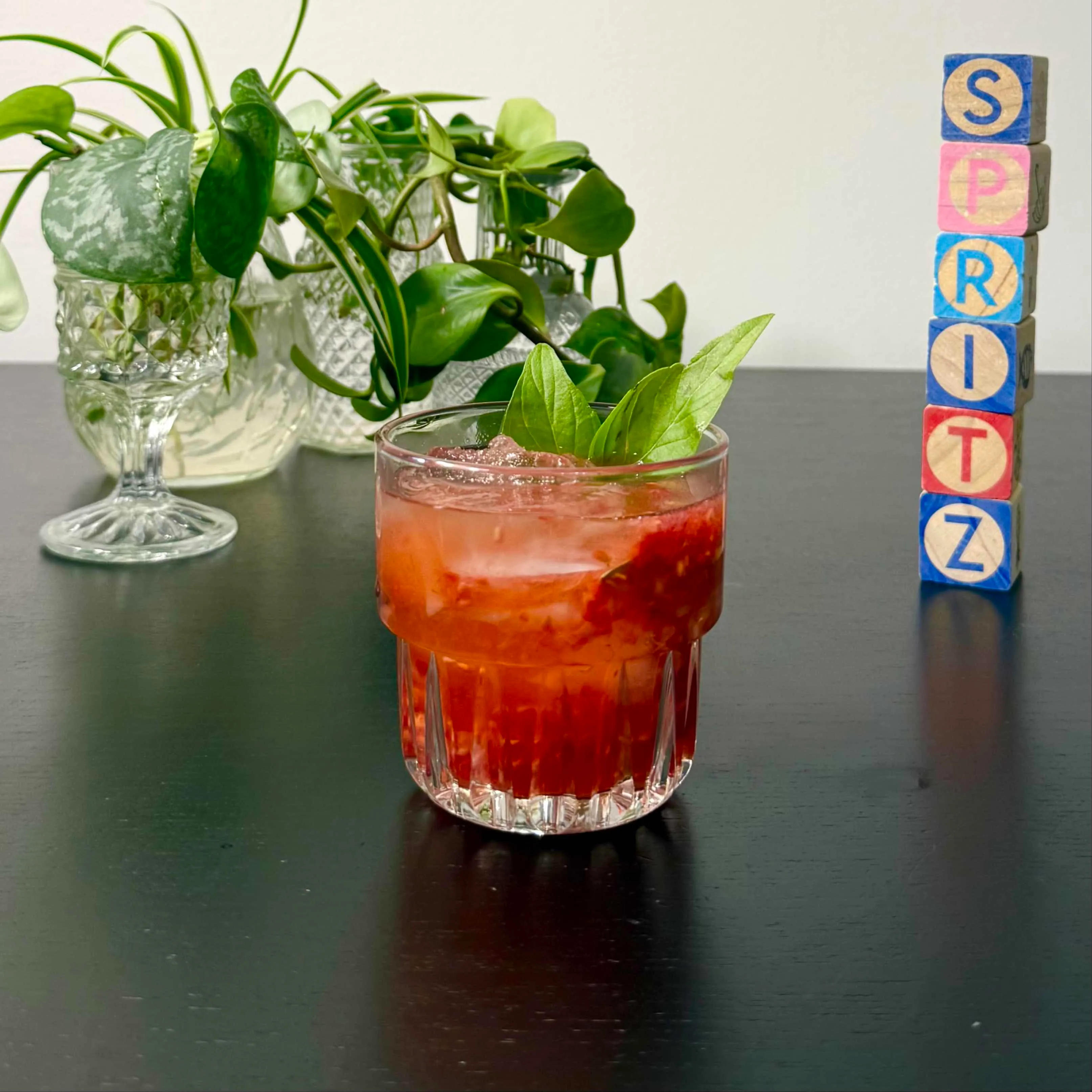 Berry Basil Smash with muddled raspberries and bourbon over ice in a rocks glass, topped with fresh basil leaves