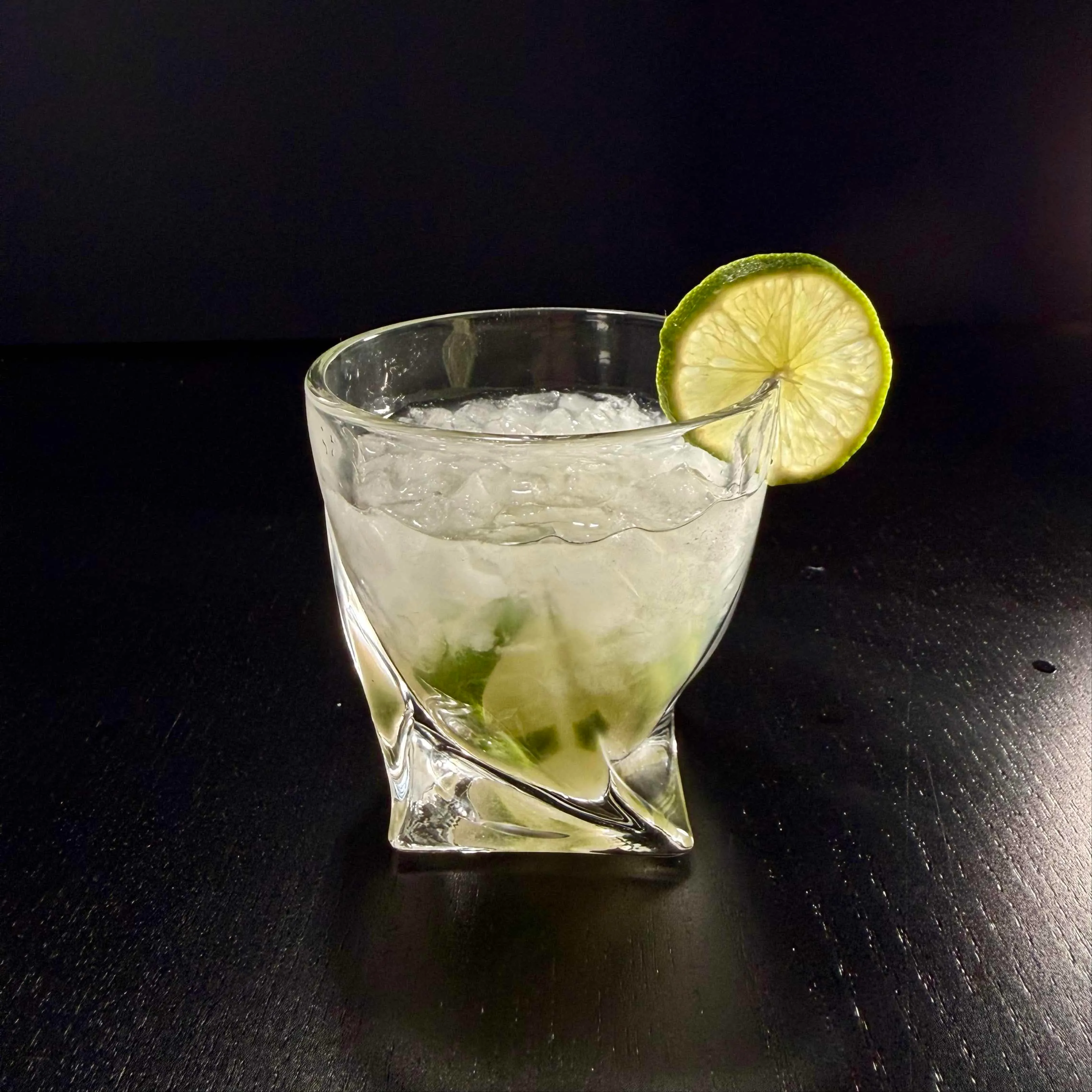 Caipirinha cocktail in a rocks glass with muddled lime, cracked ice, and a lime wheel garnish